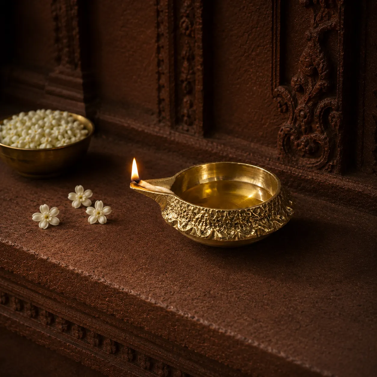 Brass Kuber deepak lit with a flame on a carved temple mantel